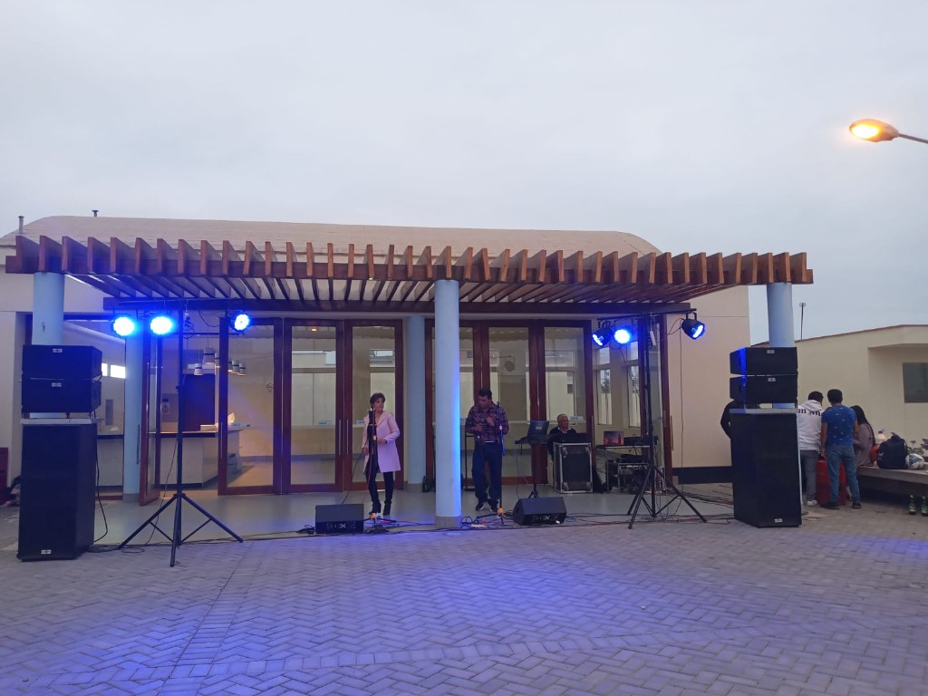 Montaje Paquete Concierto Standard: dúo en vivo bajo pérgola, sistemas PA a los lados, monitores, luces azules y consola al fondo.